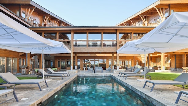 A pool area with lounge chairs and umbrellas, surrounded by wooden buildings with balconies. - Pirin Golf Hotel & SPA (Razlog)