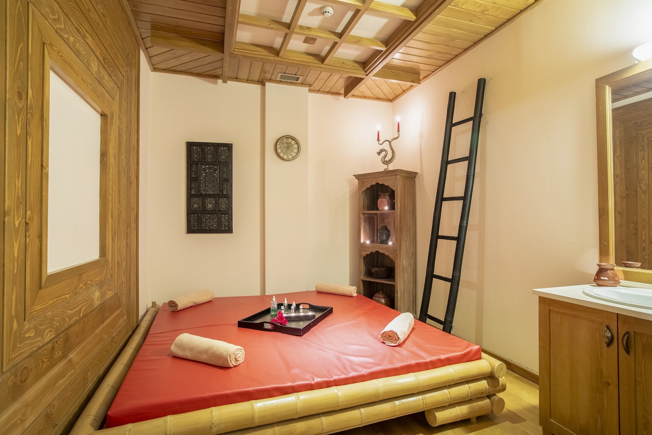 A room with a bed, a wooden cabinet, a ladder, and a wall-mounted shelf with decorative items.