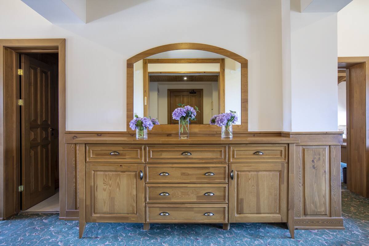 A wooden dresser with a mirror and two vases of purple flowers.