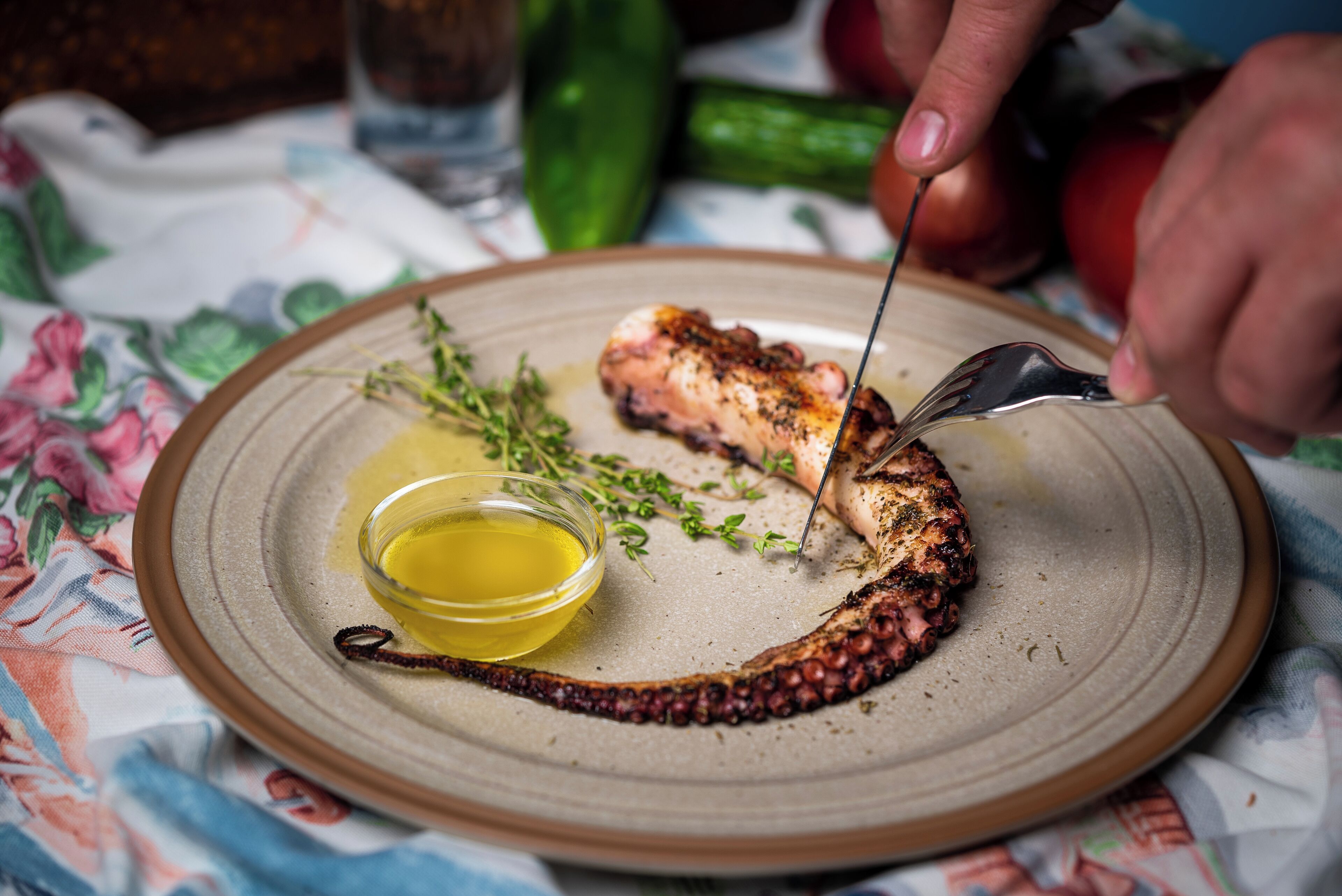 Un plato con pulpo a la parrilla, un tazón pequeño de aceite de oliva y una ramita de tomillo.
