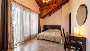 A bedroom with a wooden ceiling, a bed with a floral bedspread, a desk with a lamp, and a large mirror.