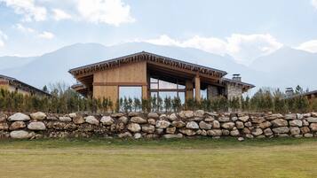 A modern building with a stone wall in front, set against a mountainous backdrop.