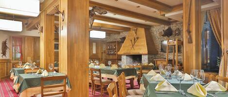Un restaurante con interiores de madera, varias mesas preparadas para comer y una chimenea de piedra.