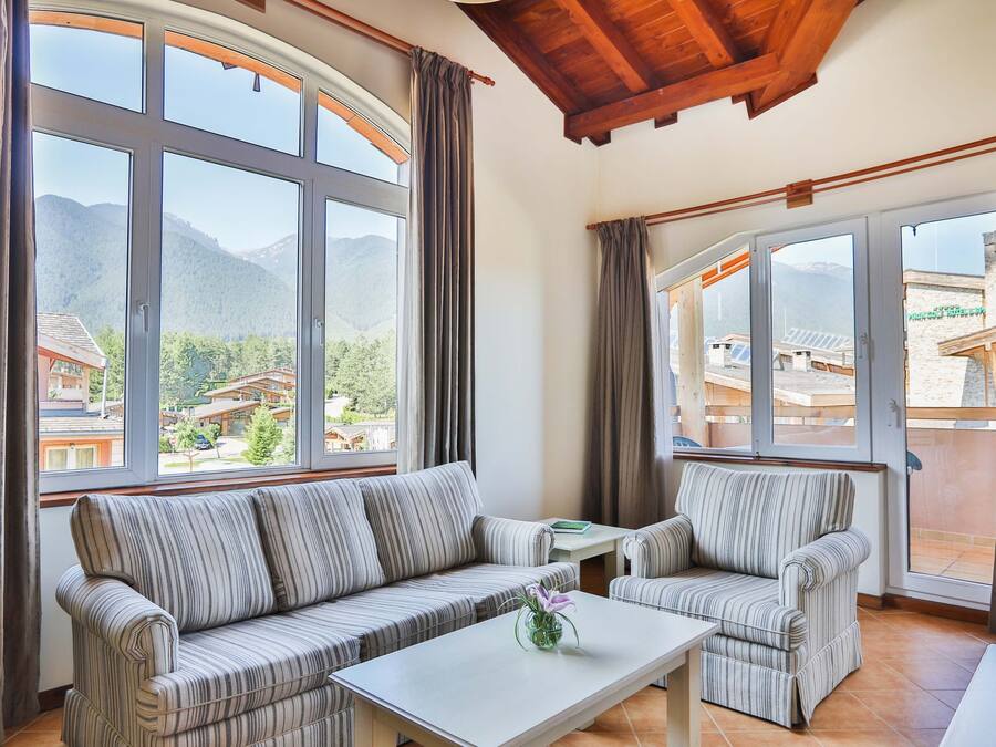 A room with a sofa set, a coffee table, and large windows offering a mountain view.