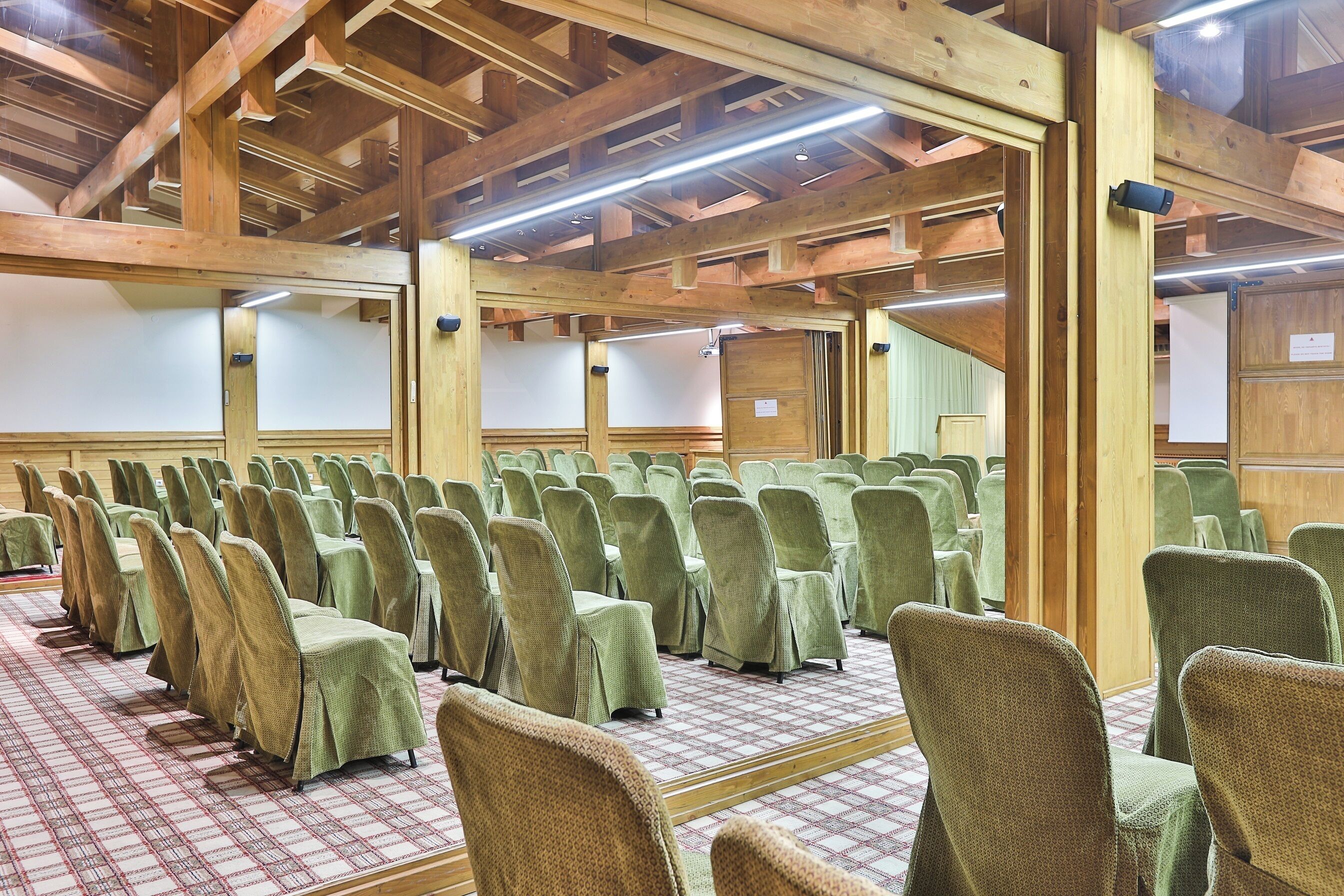 Un salón de conferencias con hileras de sillas, vigas de madera y suelo a cuadros.