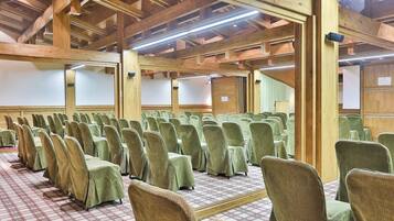 Un salón de conferencias con hileras de sillas, vigas de madera y suelo a cuadros.