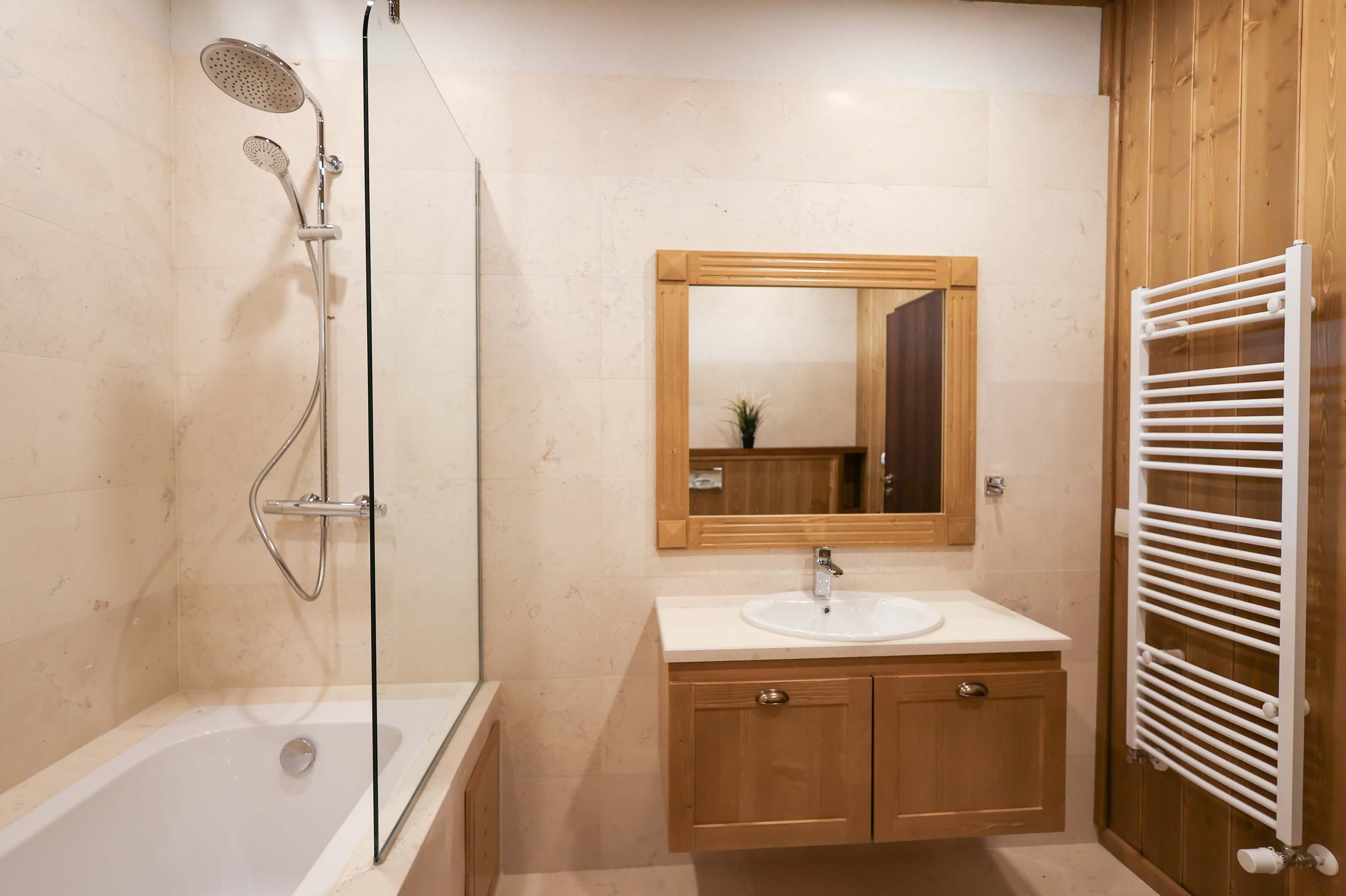 Un baño con ducha de vidrio, tocador de madera con lavabo y espejo superior.