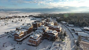 A snow-covered resort with multiple buildings, a ski slope, and a forested area in the background. - Pirin Golf & Country Club Apartment Complex (Razlog)