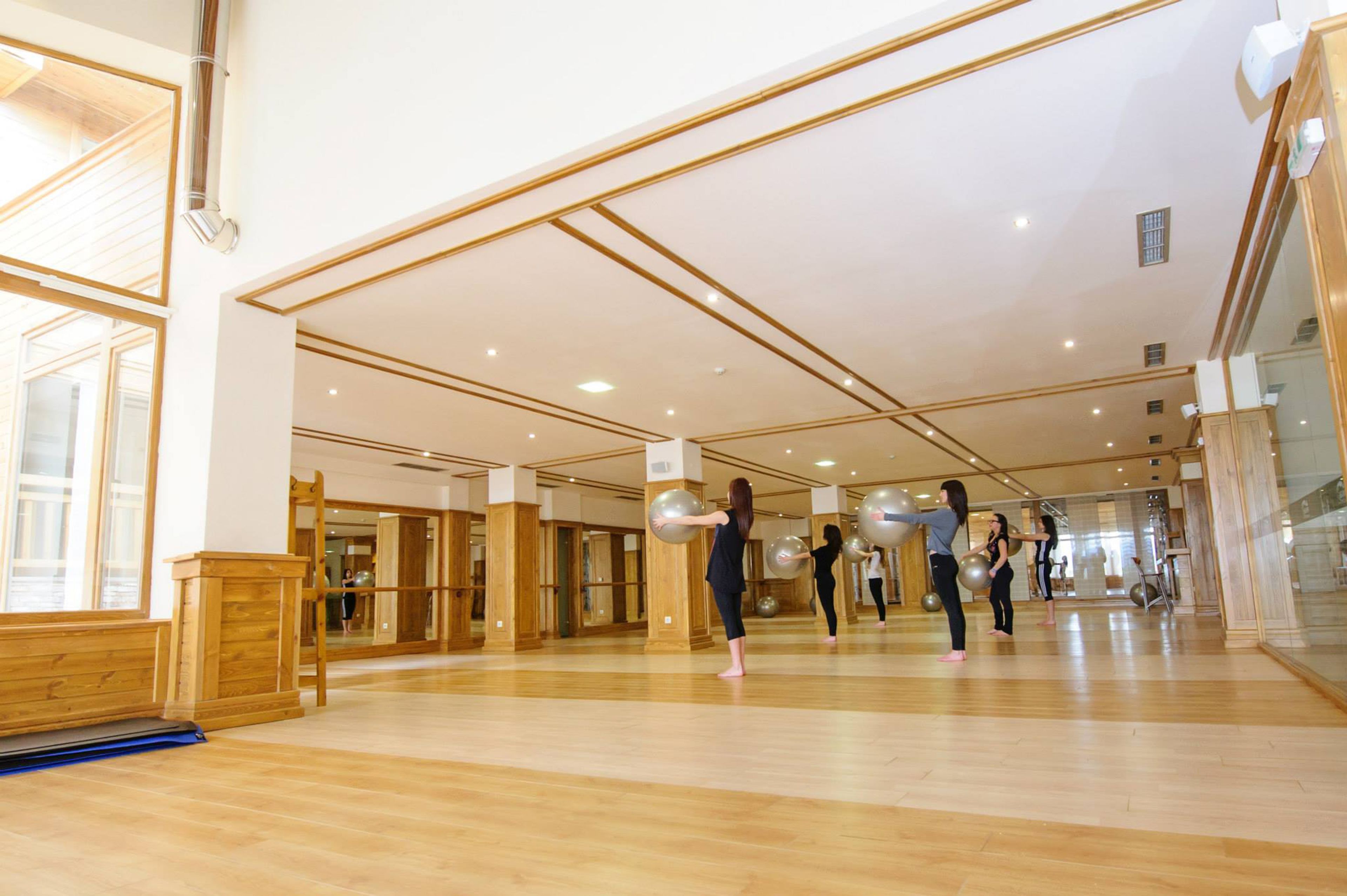 A spacious gym with wooden floors and mirrored walls, featuring exercise equipment and a large mirror.
