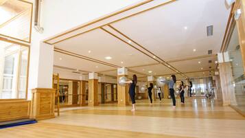 A spacious gym with wooden floors and mirrored walls, featuring exercise equipment and a large mirror.