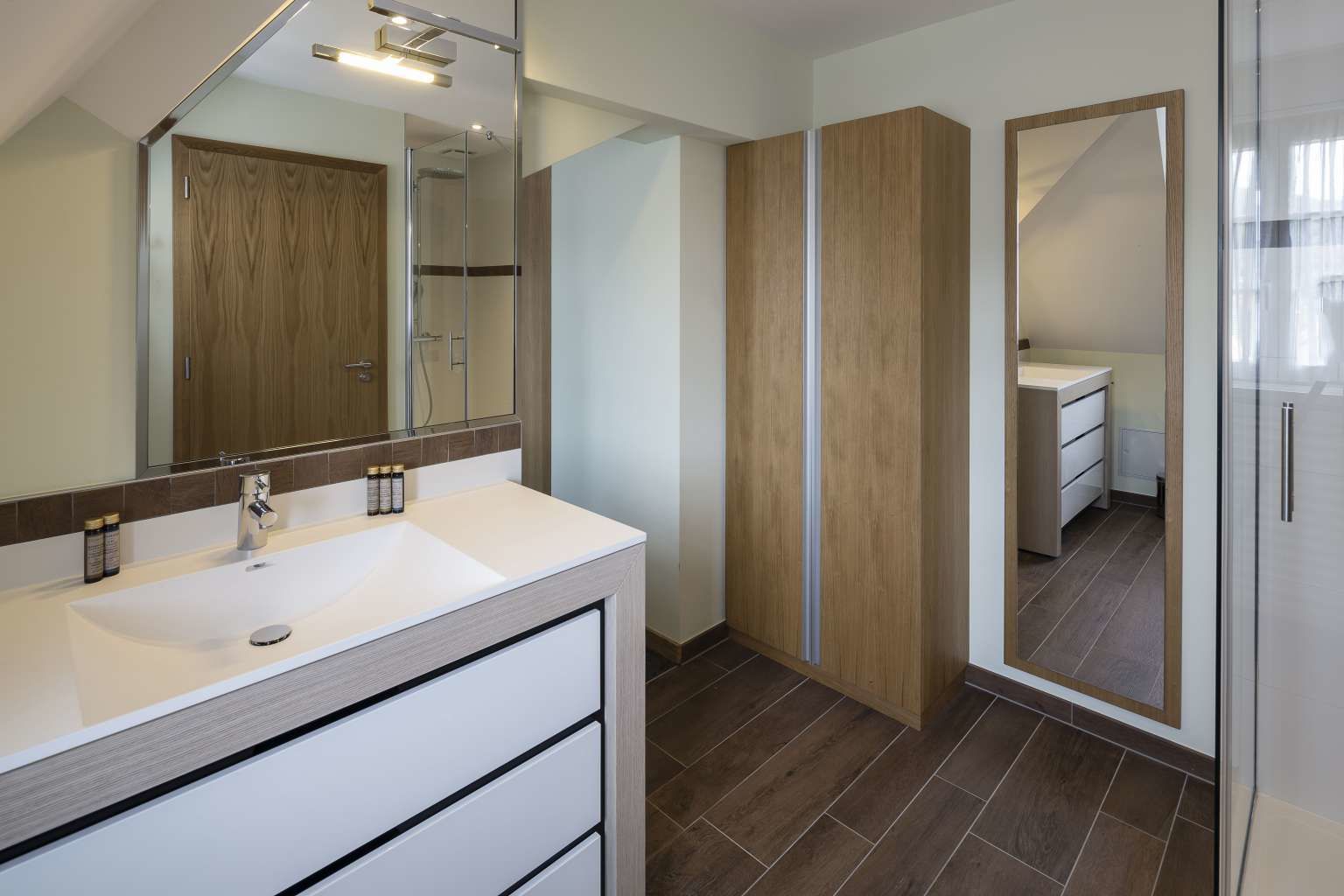 A modern bathroom with a white sink, wooden vanity, and a large mirror.