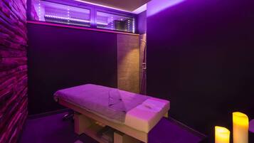 A massage room with a wooden bench, a stone wall, and purple lighting.