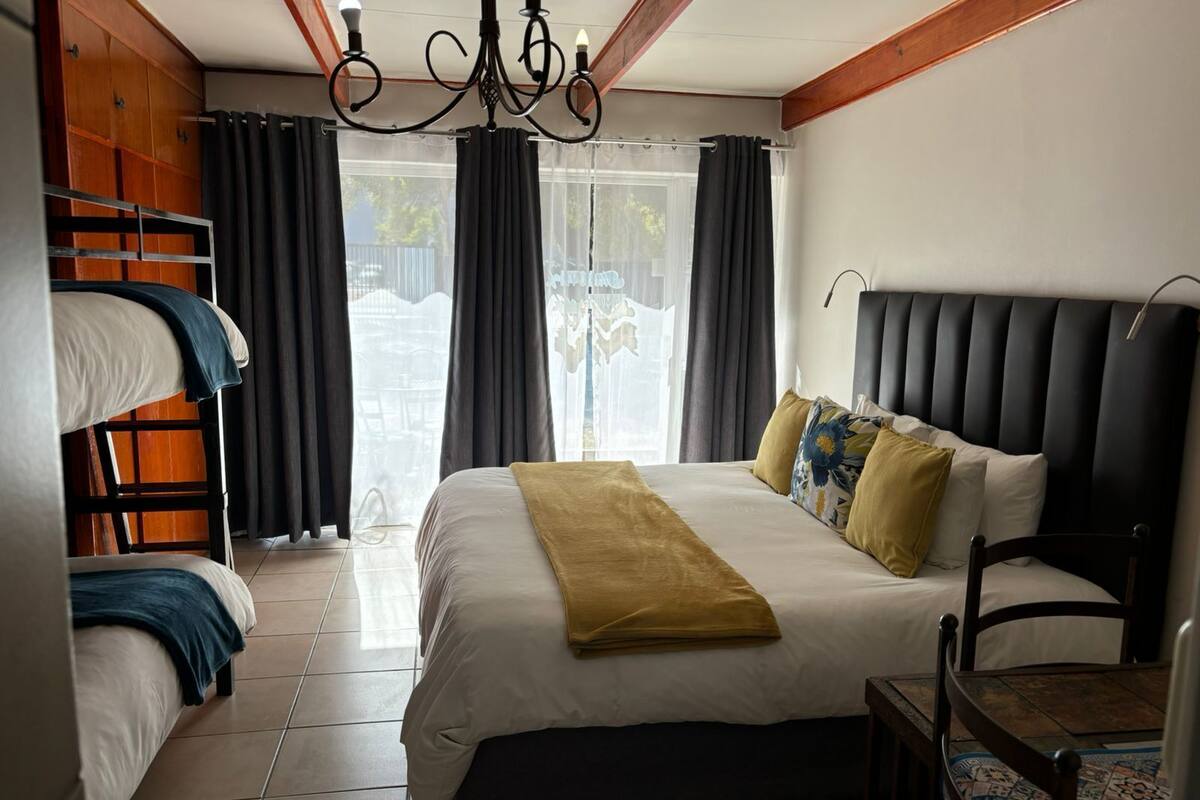 Une chambre à coucher avec un grand lit, une tête de lit en bois, un lustre et une vue sur l’extérieur par une fenêtre.