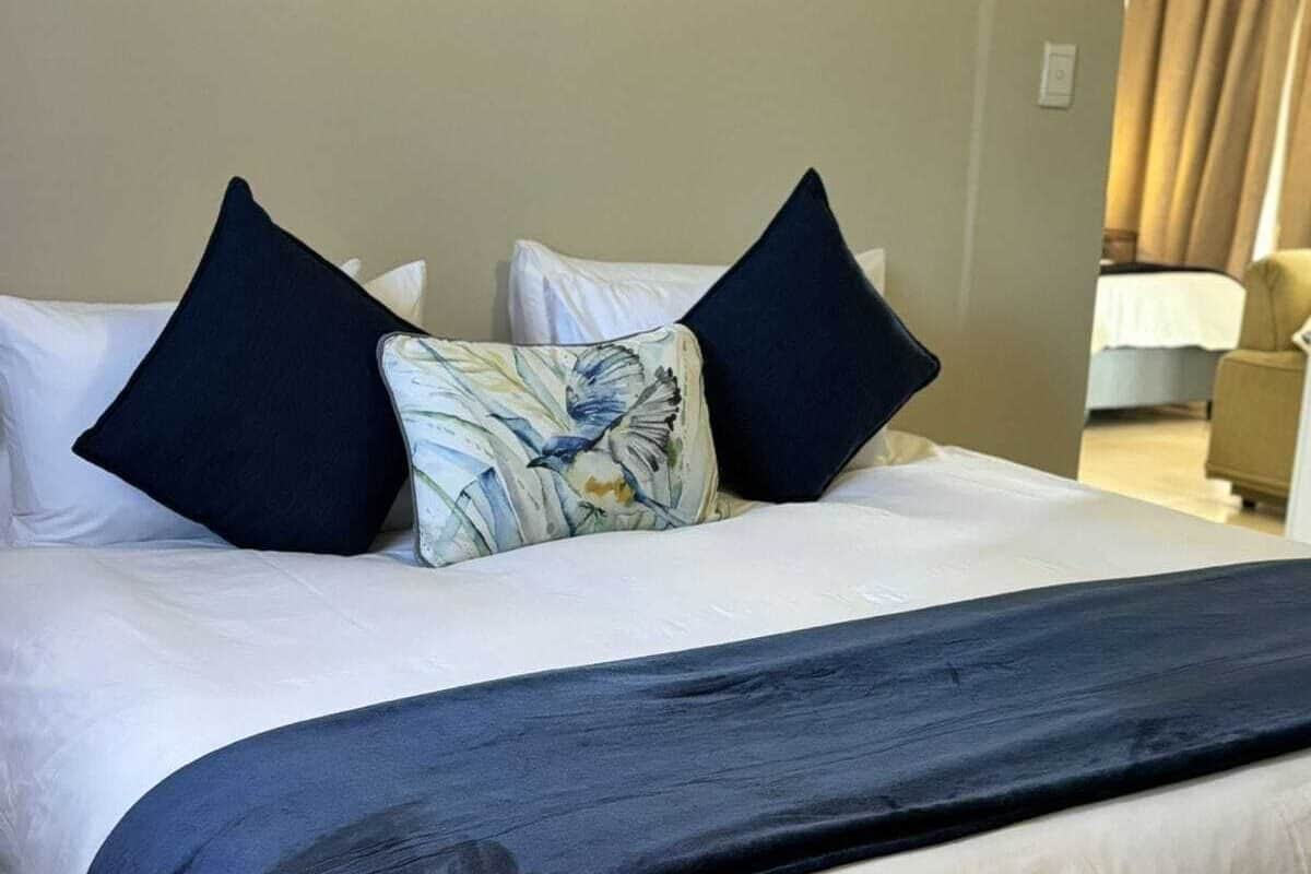 Un lit bien fait, avec du linge de lit blanc et des oreillers bleu foncé, un coussin à motifs floraux et un plaid bleu foncé.