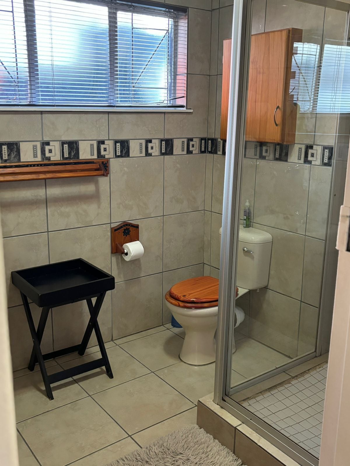 Un baño con inodoro, cabina de ducha, toallero y ventana con persianas.