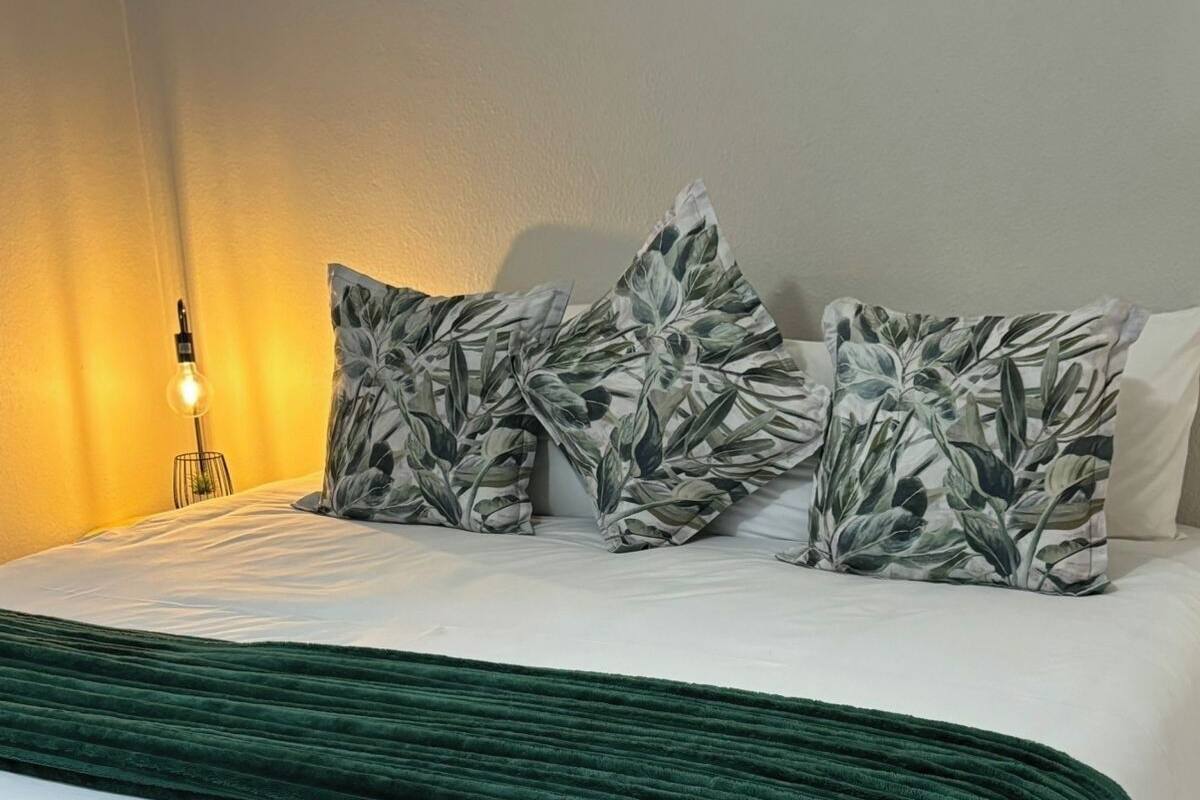 Un lit bien fait, avec une couverture verte, du linge de lit blanc et des coussins à motifs de feuilles.