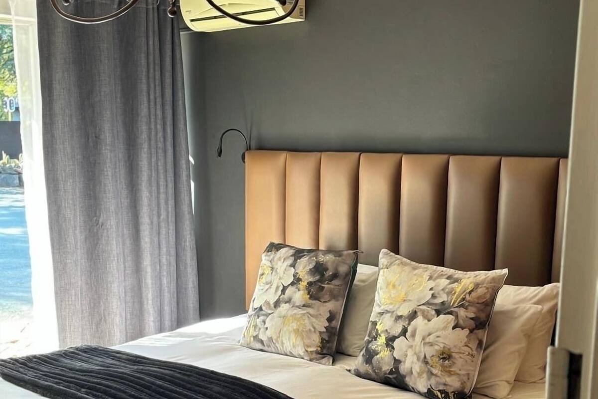 Une chambre à coucher avec un grand lit, une tête de lit et une fenêtre avec des rideaux.