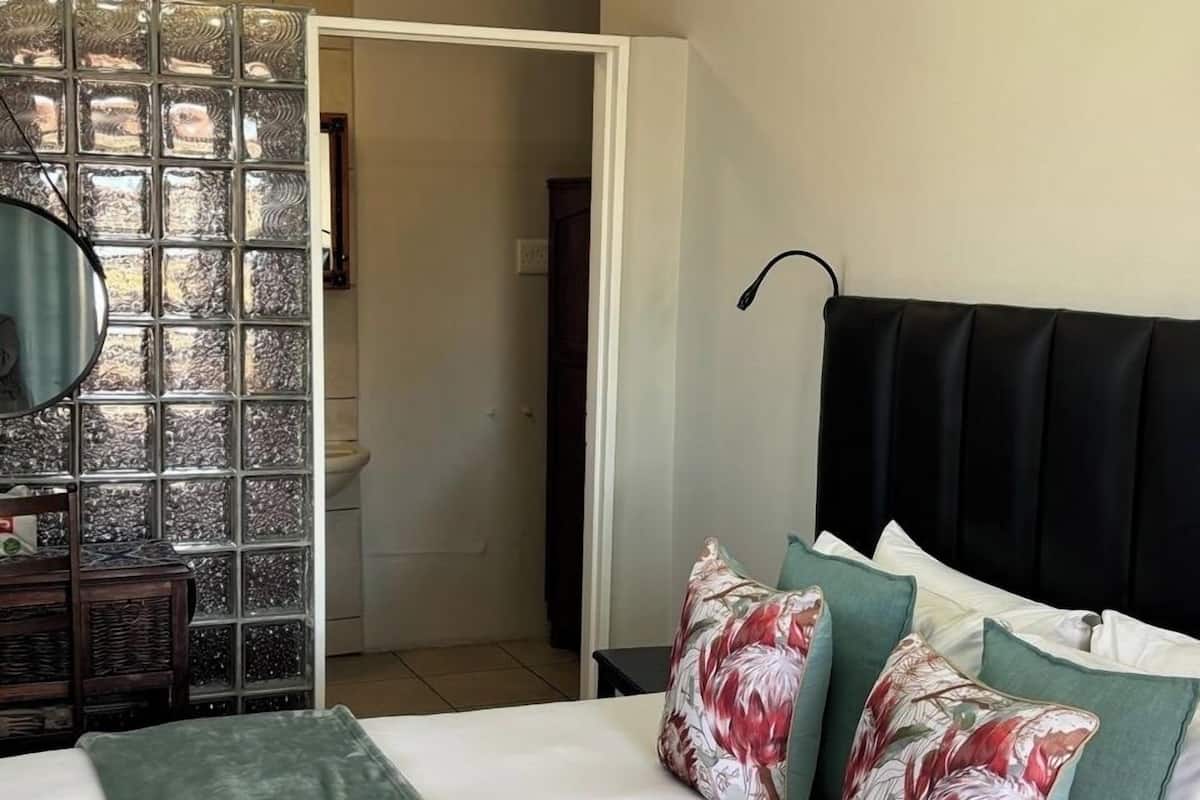Une chambre à coucher avec un lit, des oreillers, une table de chevet, un miroir et une vue sur la salle de bain.