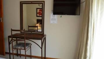 Una habitación con un escritorio de madera, una silla, un espejo, un televisor de pantalla plana y una cortina.