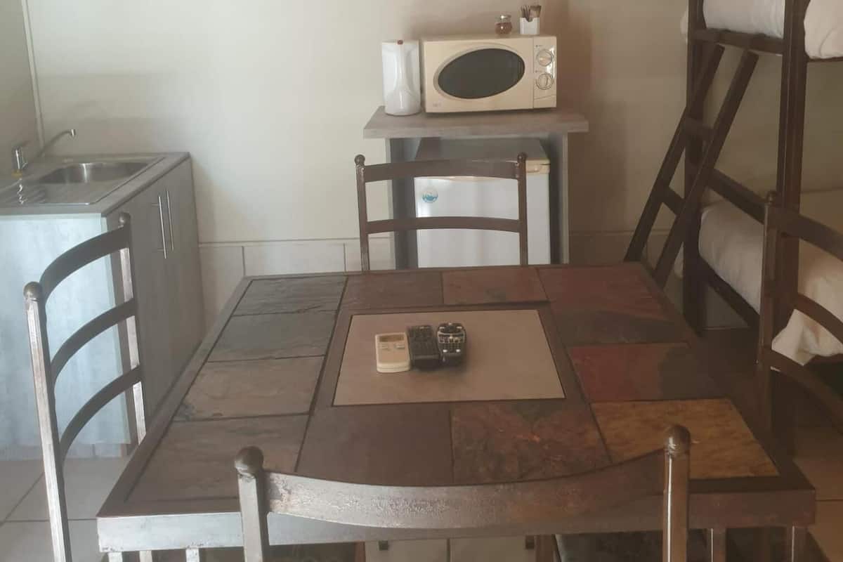 Une petite cuisine équipée d’un micro-ondes, d’un évier et d’un placard. On y trouve deux chaises et une table sur laquelle est posée une télécommande.