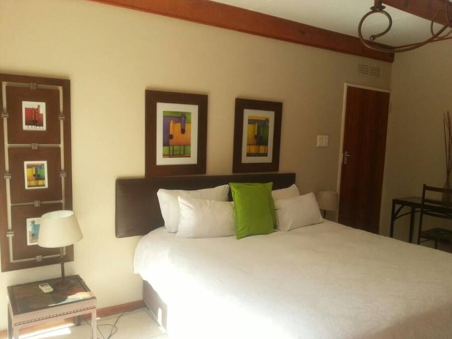 A hotel room with a large bed, a nightstand with a lamp, and framed artwork on the wall.