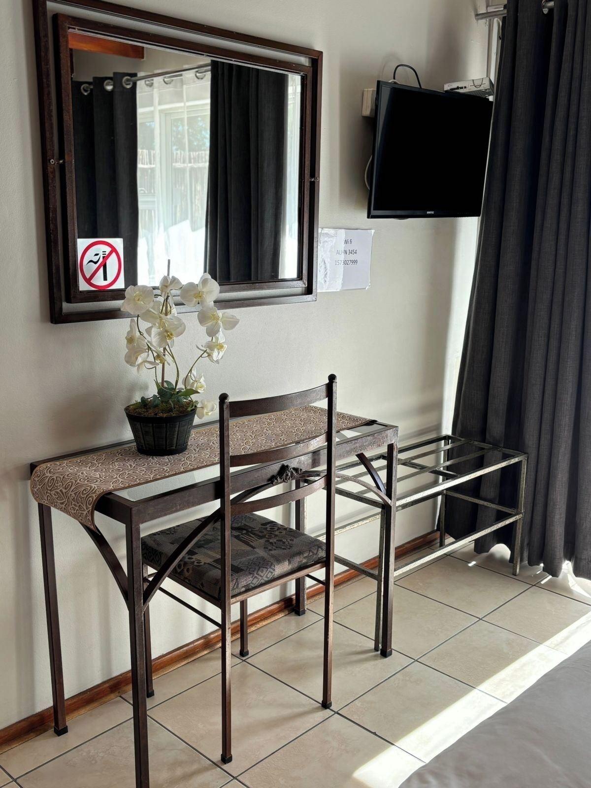 Habitació amb escriptori, cadira, planta en test, mirall, televisió i finestra amb cortines.