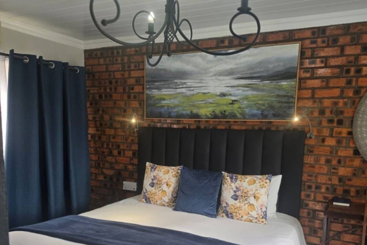 Une chambre à coucher avec un grand lit, un mur en briques, un tableau et un lustre.