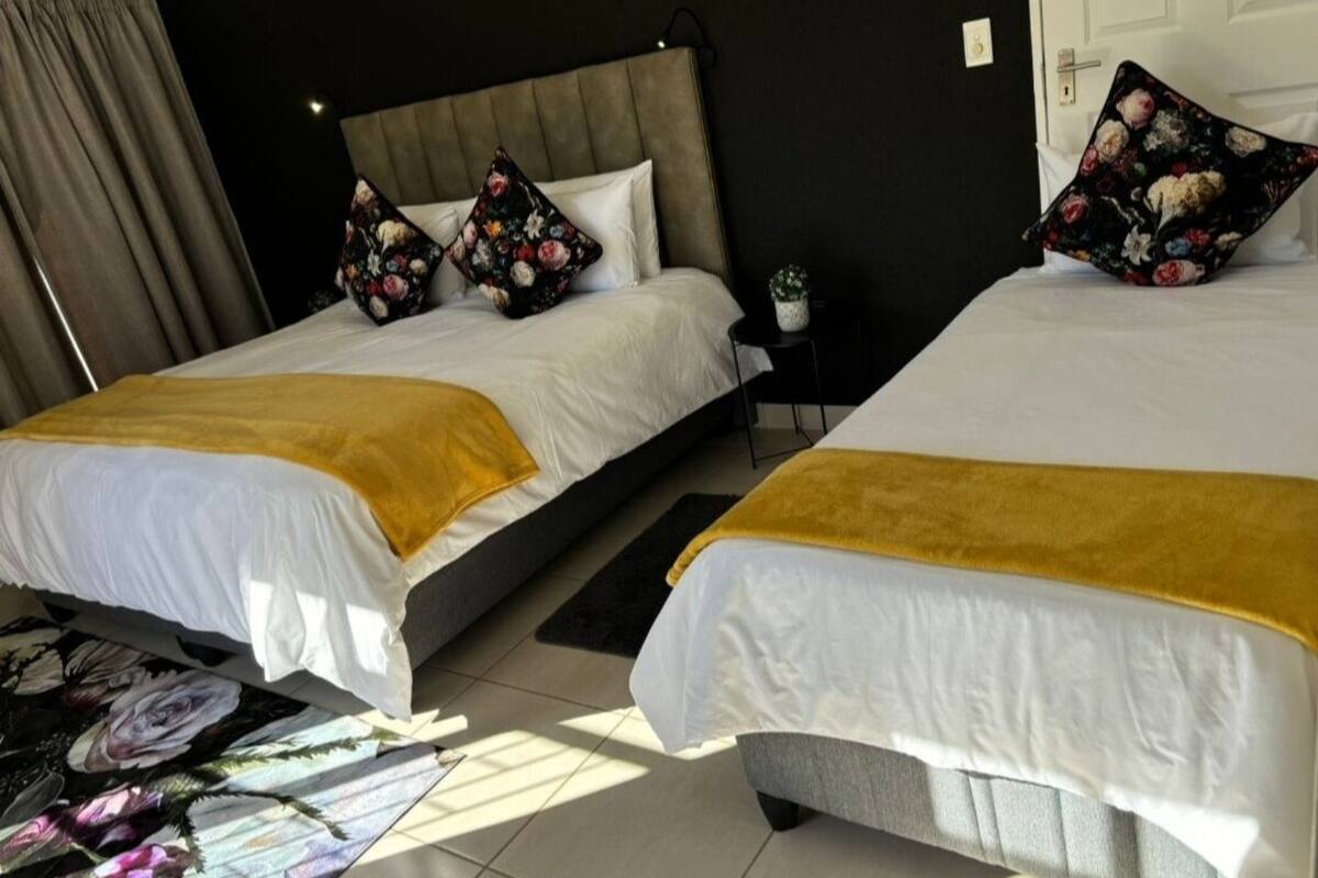 Une chambre d’hôtel avec deux lits, chacun recouvert d’un plaid jaune, doté d’une tête de lit et agrémenté d’oreillers à motifs floraux.