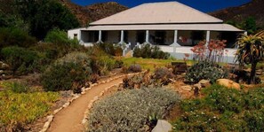 A modern building with a flat roof and a covered porch, surrounded by a landscaped garden with various plants and a winding path. - Cedar Falls (Willowmore)