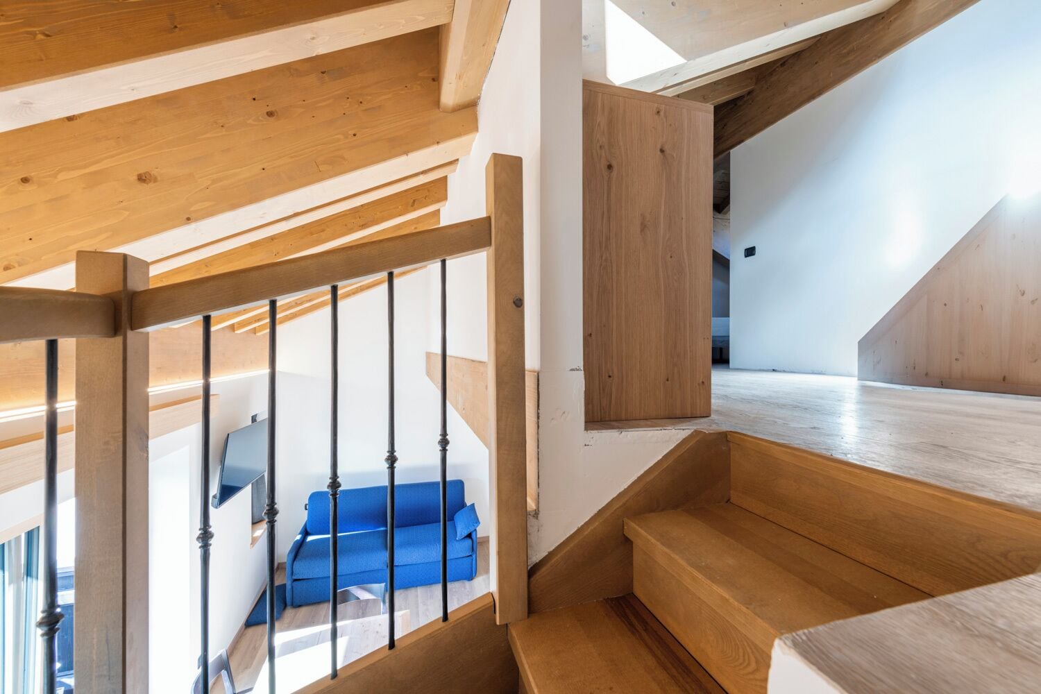 Un escalier en bois, avec un canapé bleu sur la plateforme du dernier étage.