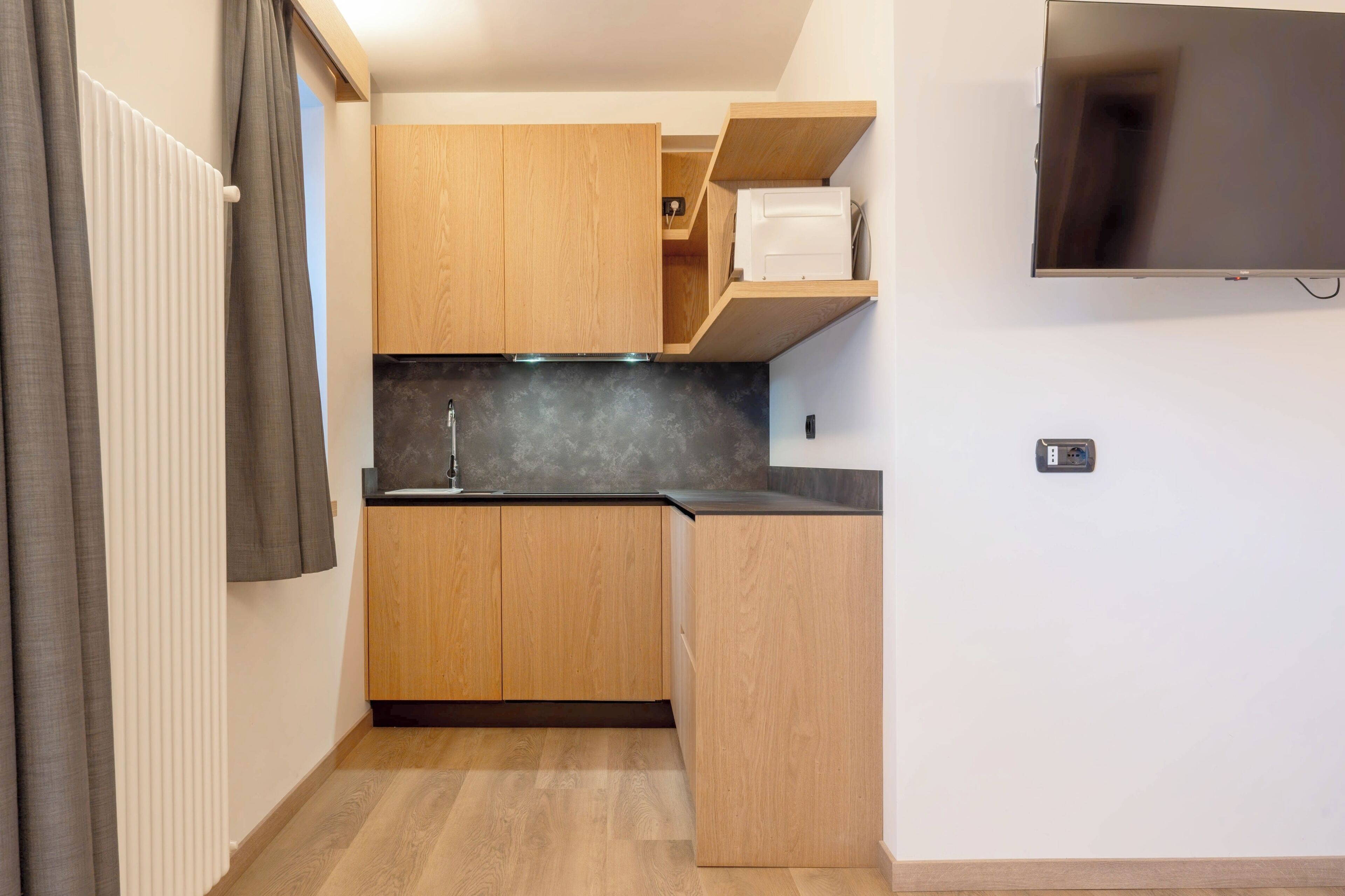 Una cocina compacta con armarios de madera, encimera negra y televisor integrado.