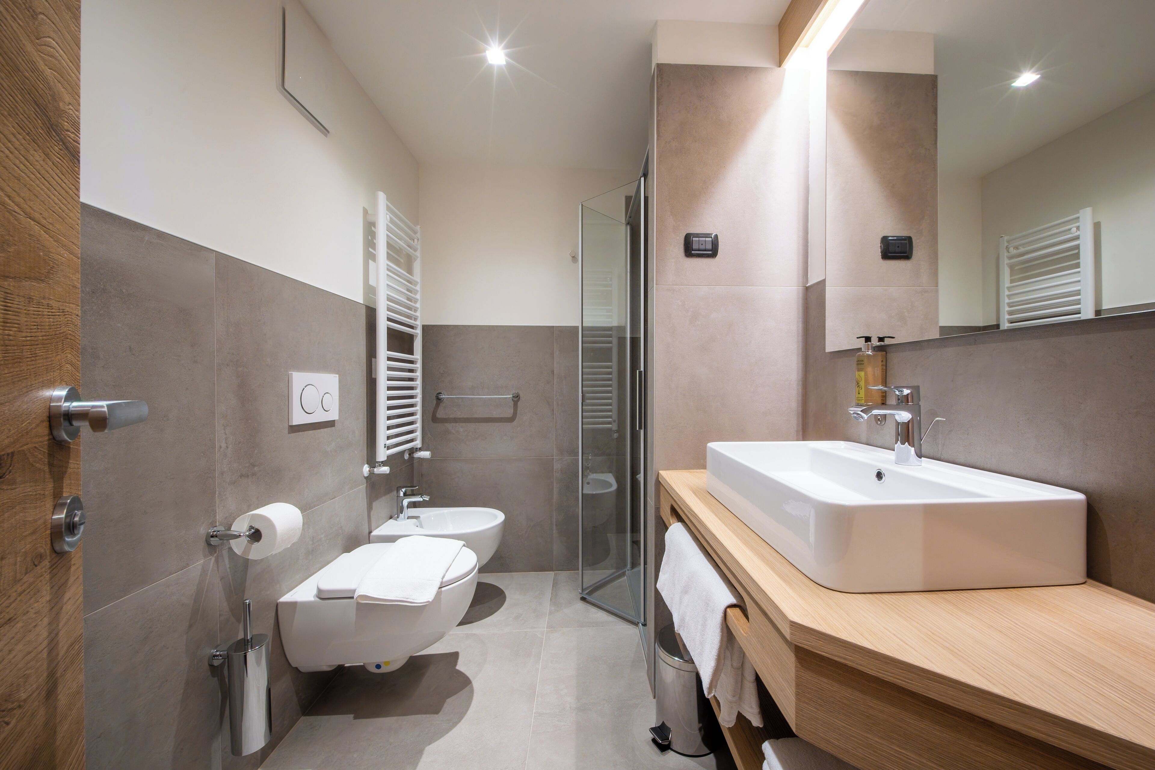 A modern bathroom with a large sink, two toilets, a glass shower enclosure, and wooden cabinetry.