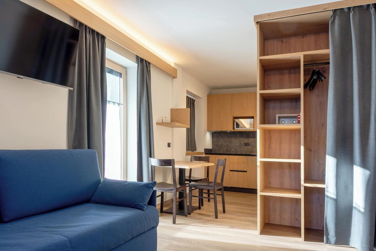 Un soggiorno moderno con un divano blu, un'area pranzo con tavolo e sedie, una cucina con mobili in legno e una cabina armadio con scaffali.