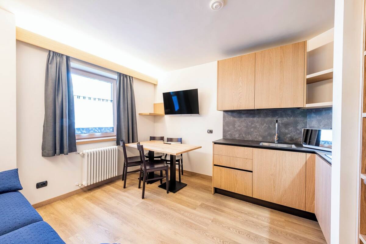 Un angolo cottura compatto con mobili in legno, un forno a microonde integrato e una finestra con tende.