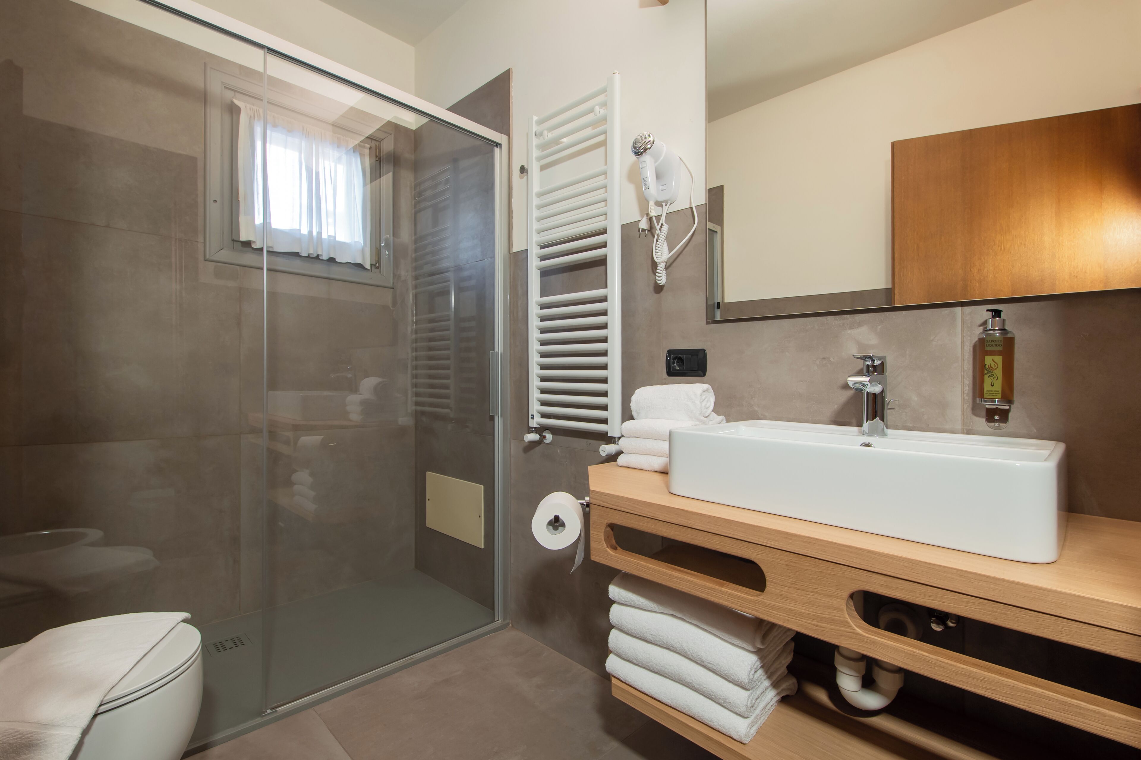 Un baño moderno con ducha envuelta en vidrio, tocador de madera con lavamanos y toallero.