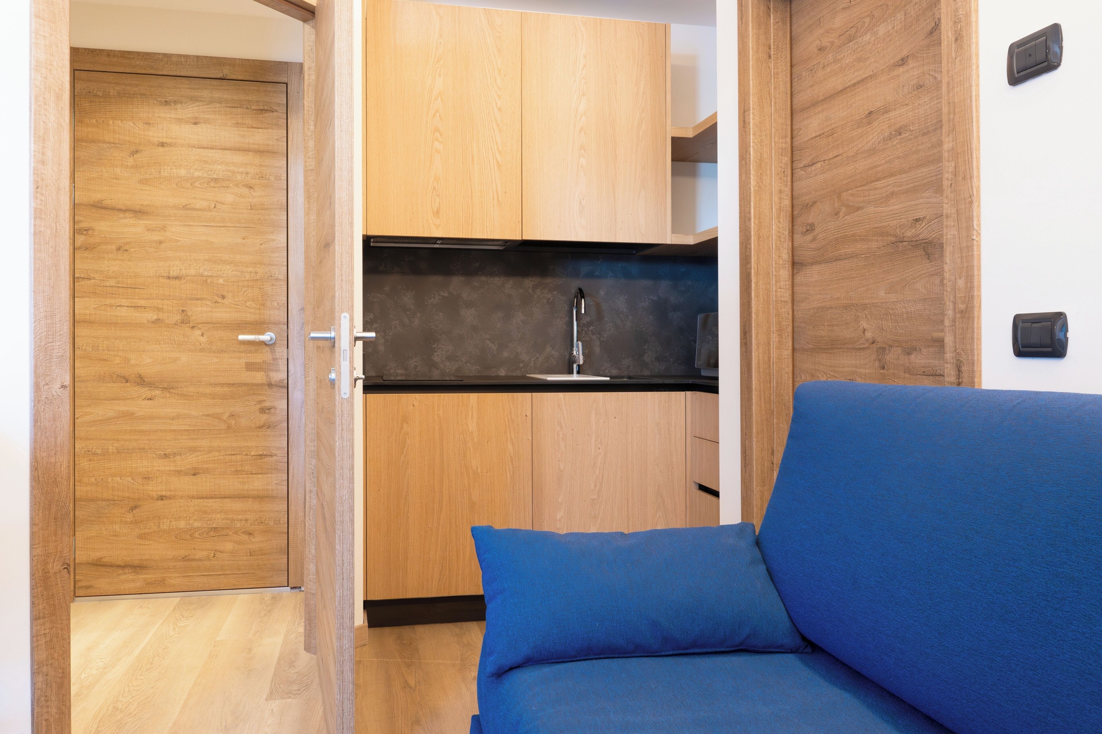 A compact living space with a kitchenette, a wooden door, and a blue sofa.