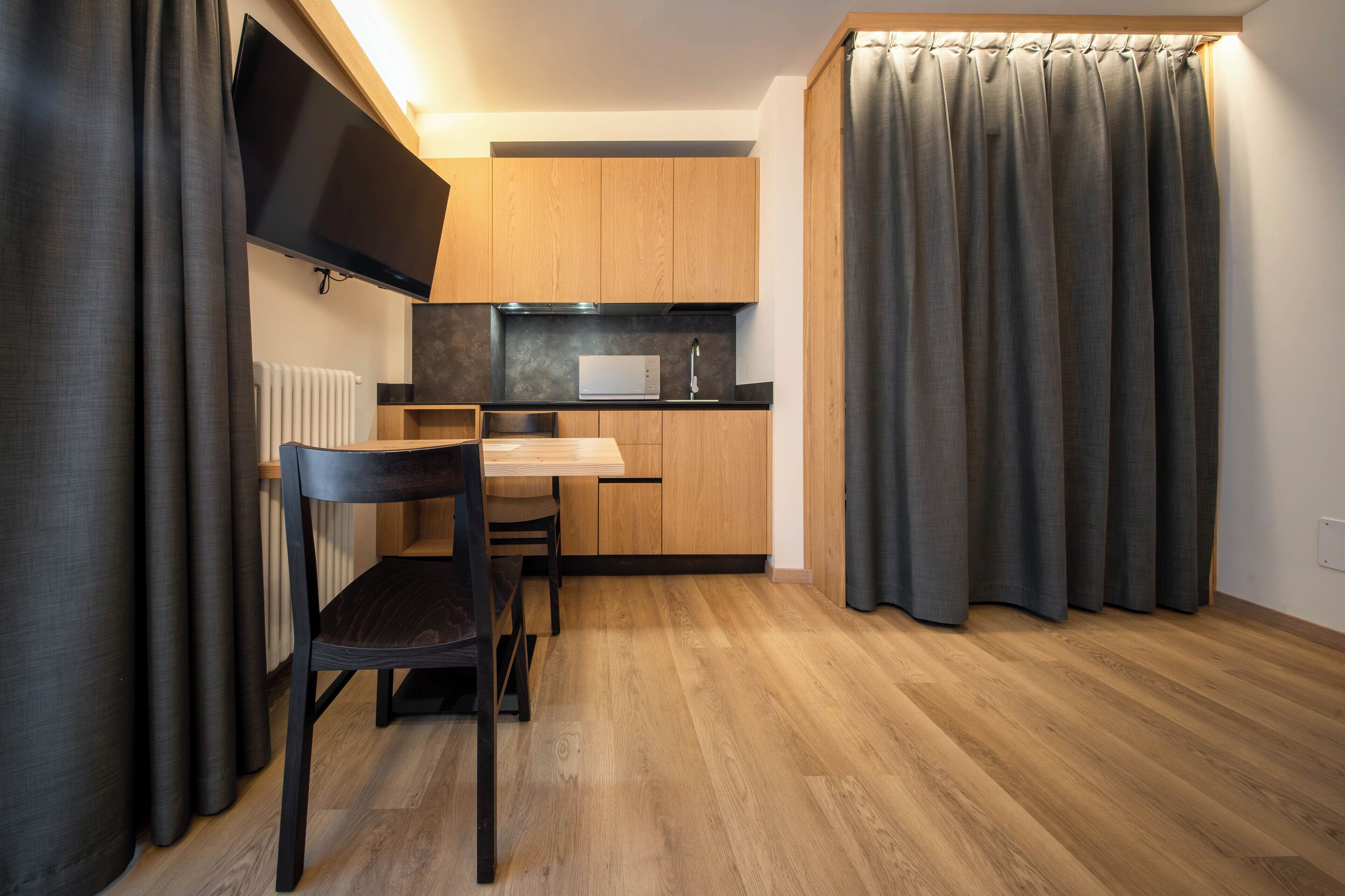 Cocina compacta con muebles de madera, microondas y comedor con una silla.