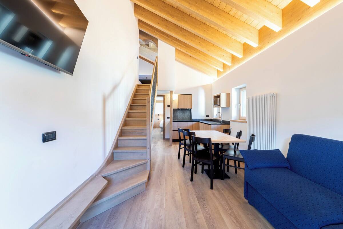Un interno moderno con una scala che conduce a una zona mansardata, un tavolo da pranzo con sedie e un divano blu.
