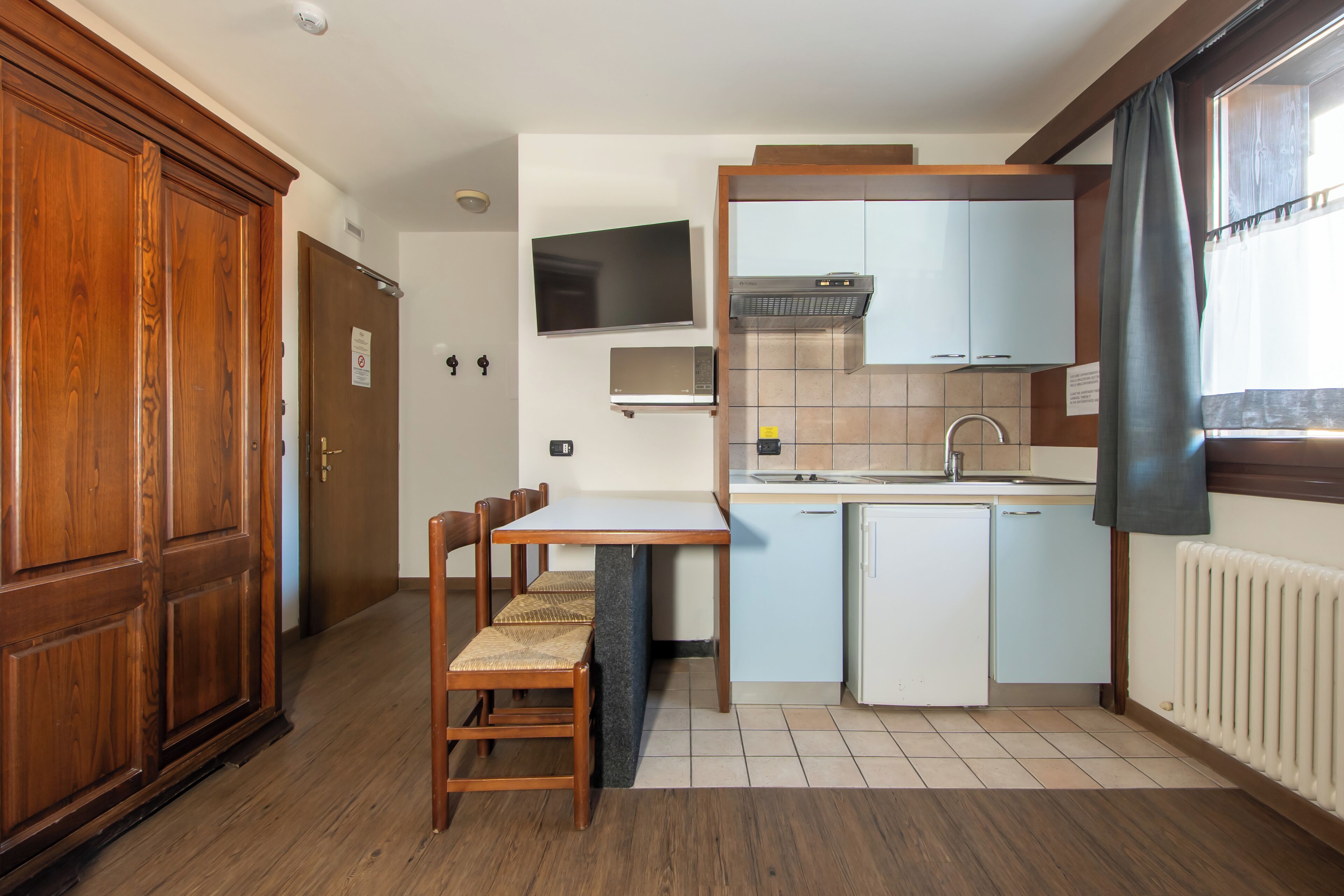 A compact kitchen with a dining table, chairs, a microwave, a small refrigerator, and a built-in oven.