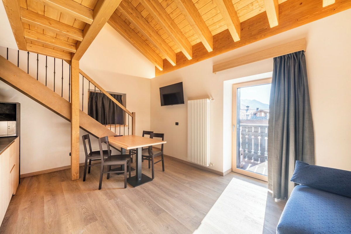 Una sala moderna con una escalera de madera, una mesa de comedor con sillas, un sofá y un ventanal con cortinas.