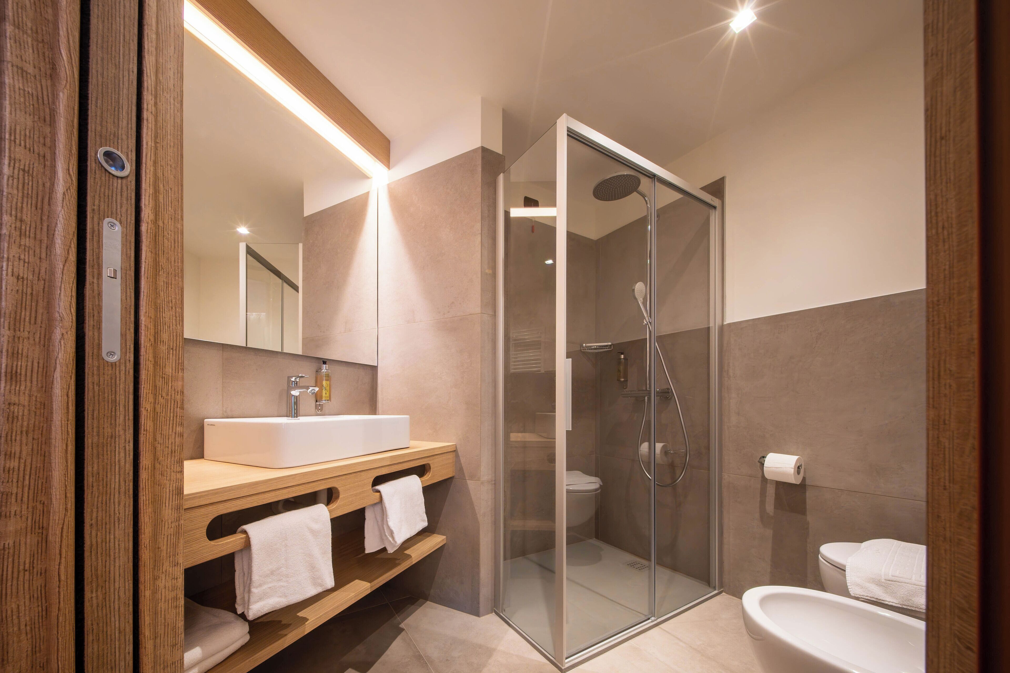 A modern bathroom with a glass-enclosed shower, a wooden vanity with a sink and towel rack, and a toilet.