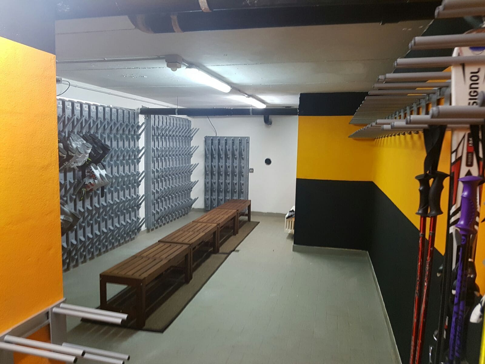Ein Zimmer mit einem an der Wand befestigten Skiständer, einer Holzbank und einer Bank mit Metallgestell.