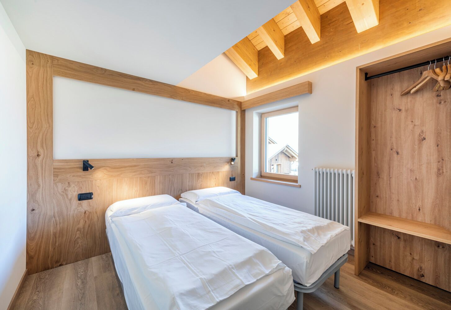 Un dormitorio con dos camas individuales, cabecero de madera, una ventana y un radiador.