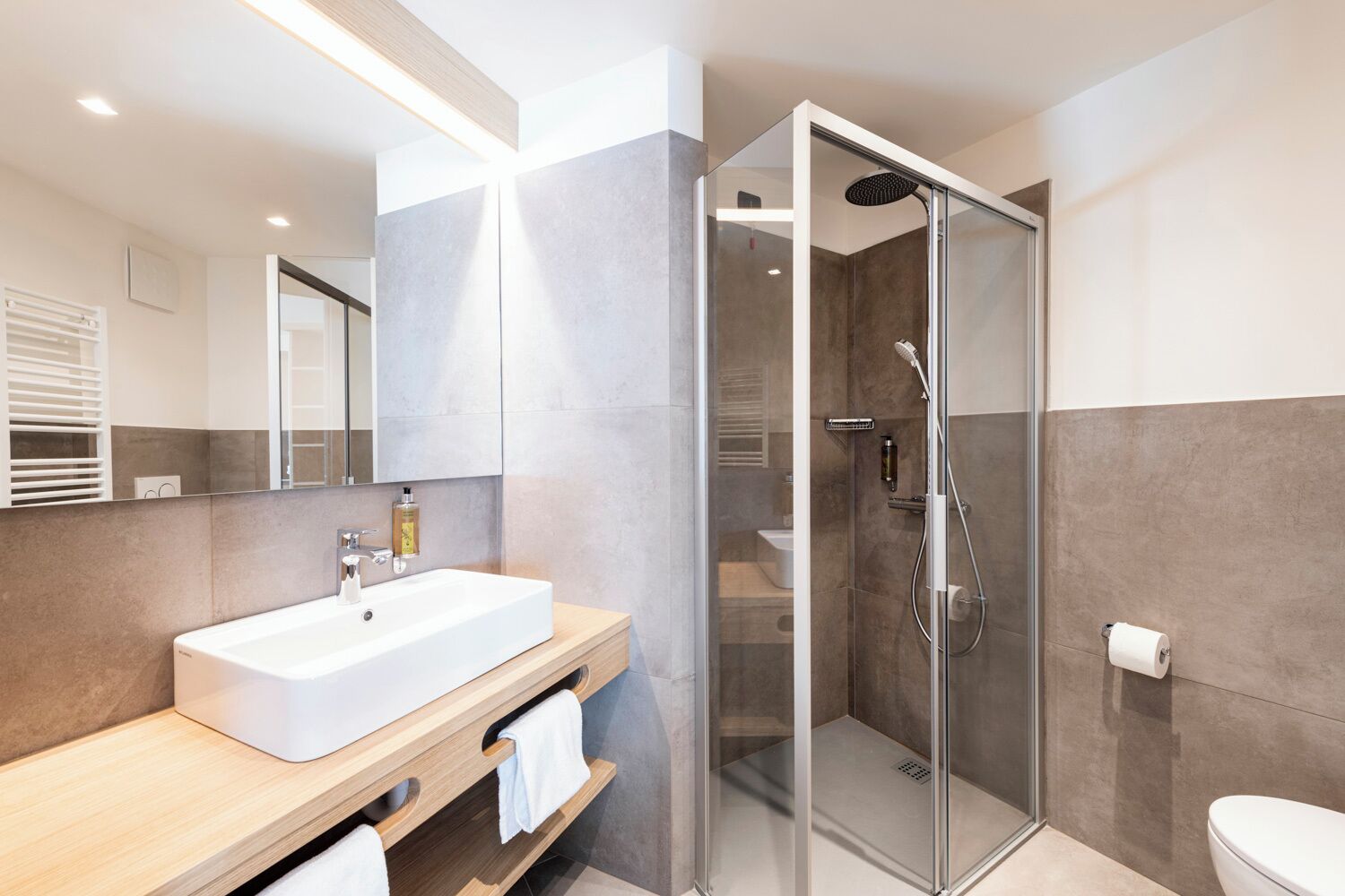 A modern bathroom with a glass-enclosed shower, a white sink, and a wooden vanity.