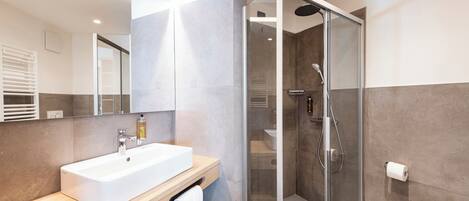 A modern bathroom with a glass-enclosed shower, a white sink, and a wooden vanity.