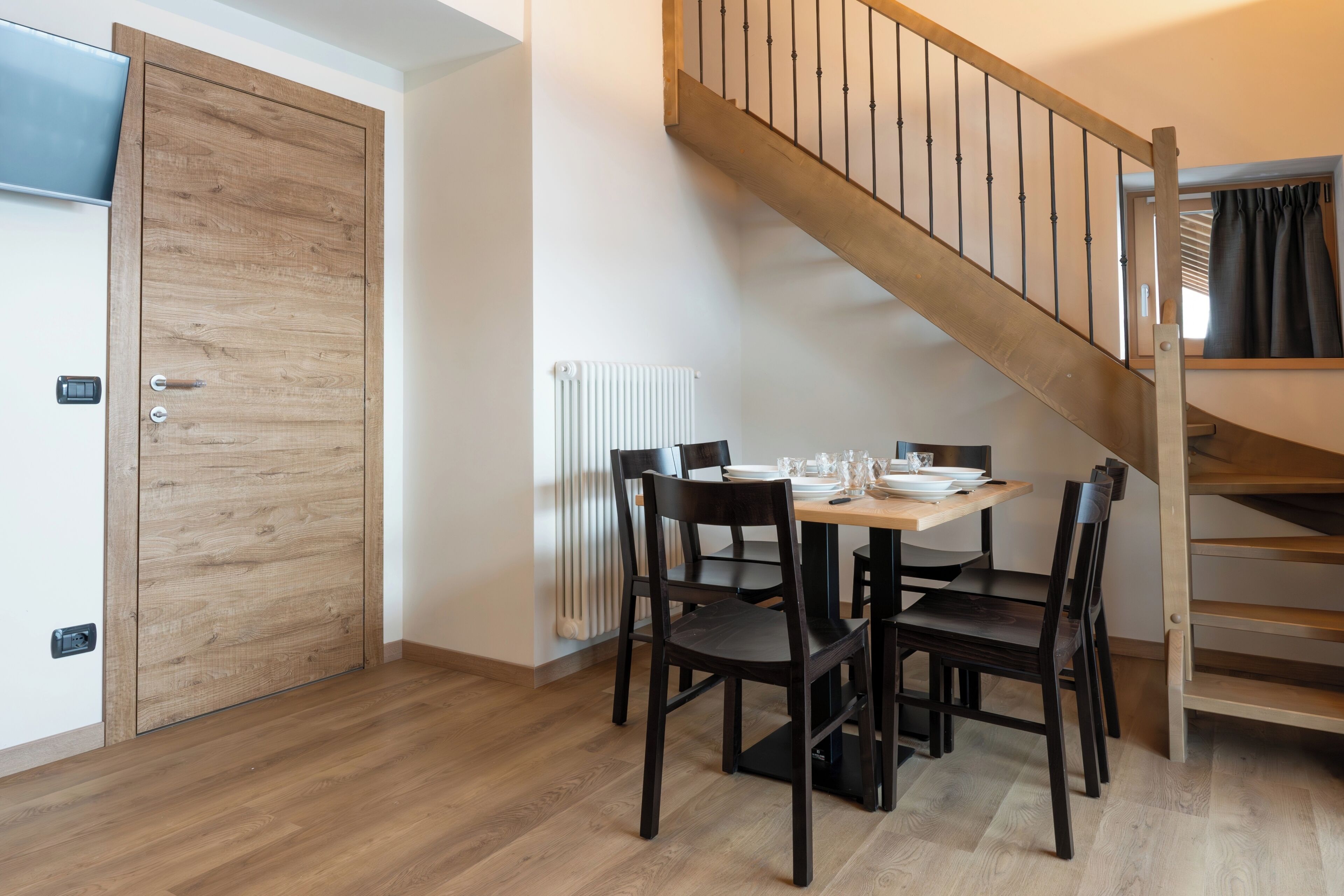 A dining area with a wooden table and chairs, a staircase, and a radiator.