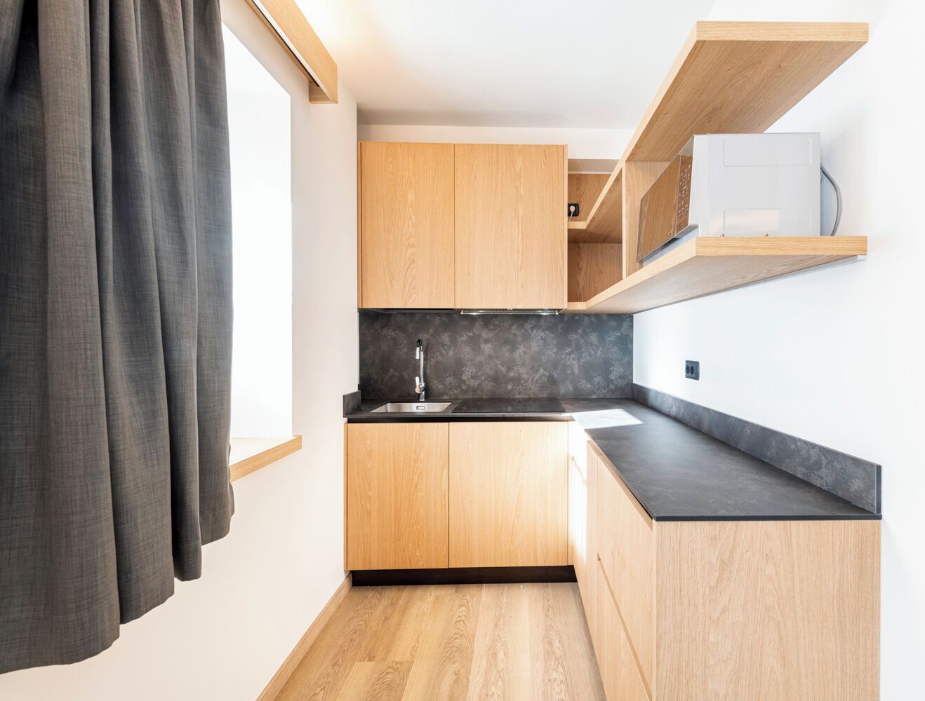 A compact kitchen with wooden cabinets, a black countertop, and a built-in microwave.