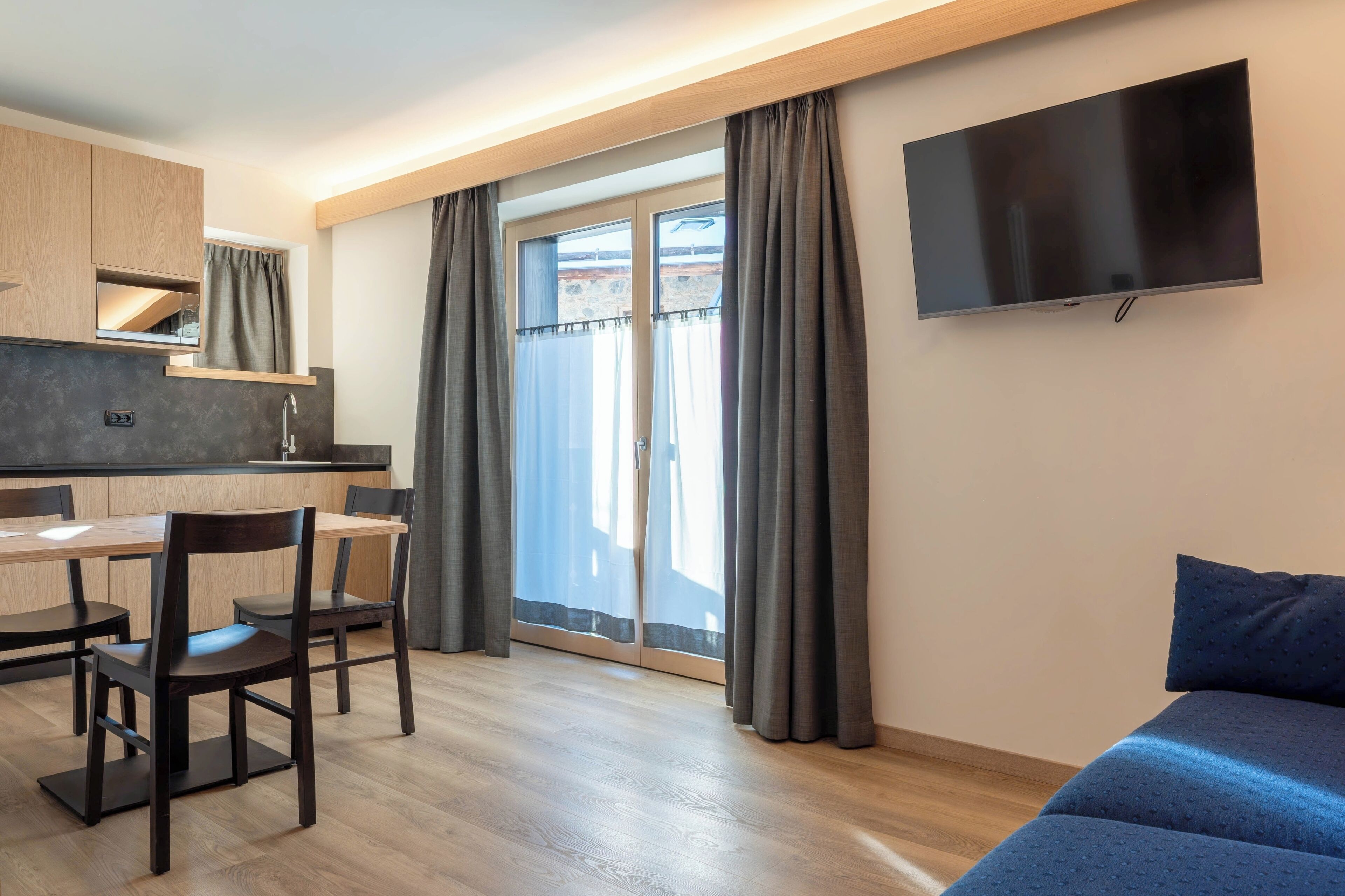 Habitación moderna con una mesa de comedor de madera, sillas, un sofá, un televisor de pantalla plana y un ventanal con cortinas.