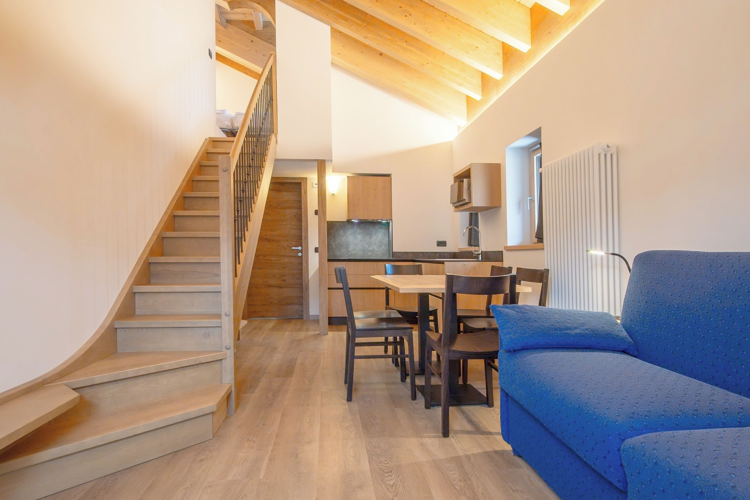 A modern interior with a staircase, a dining area, and a blue sofa.
