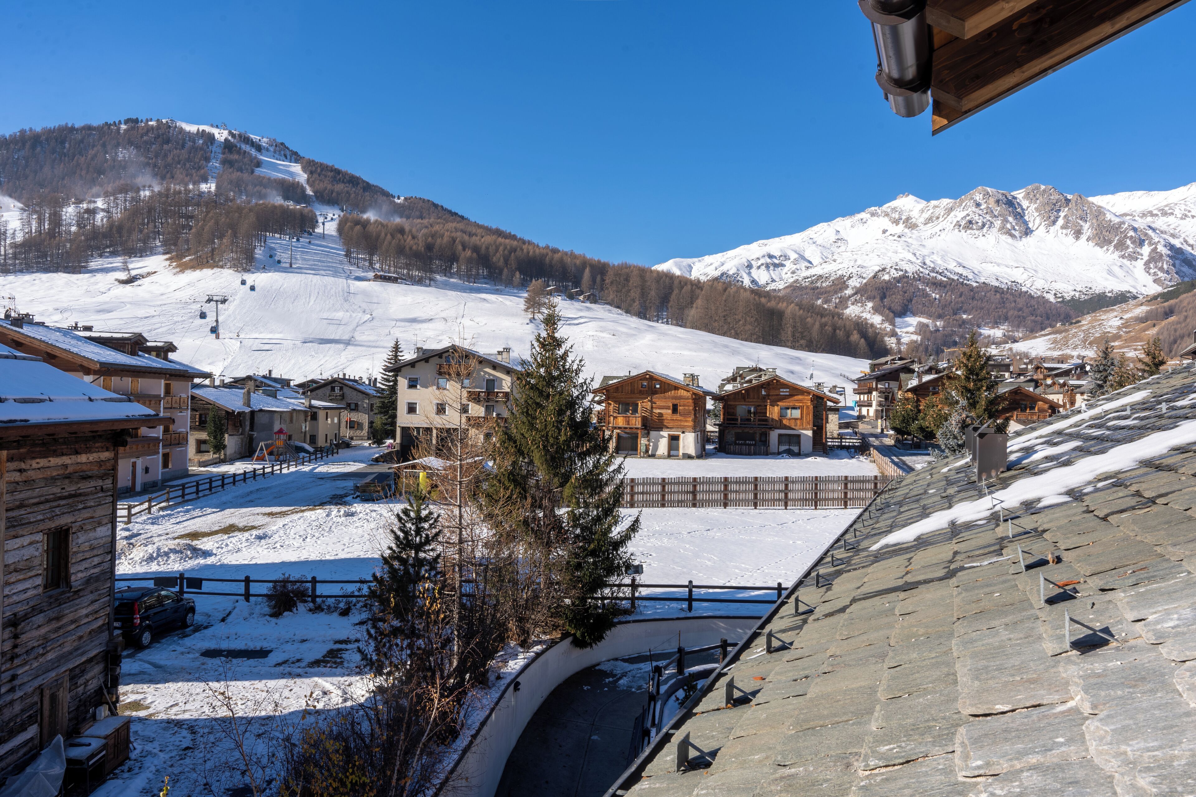 A snow-covered mountain village with wooden buildings, a ski slope, and a clear blue sky.